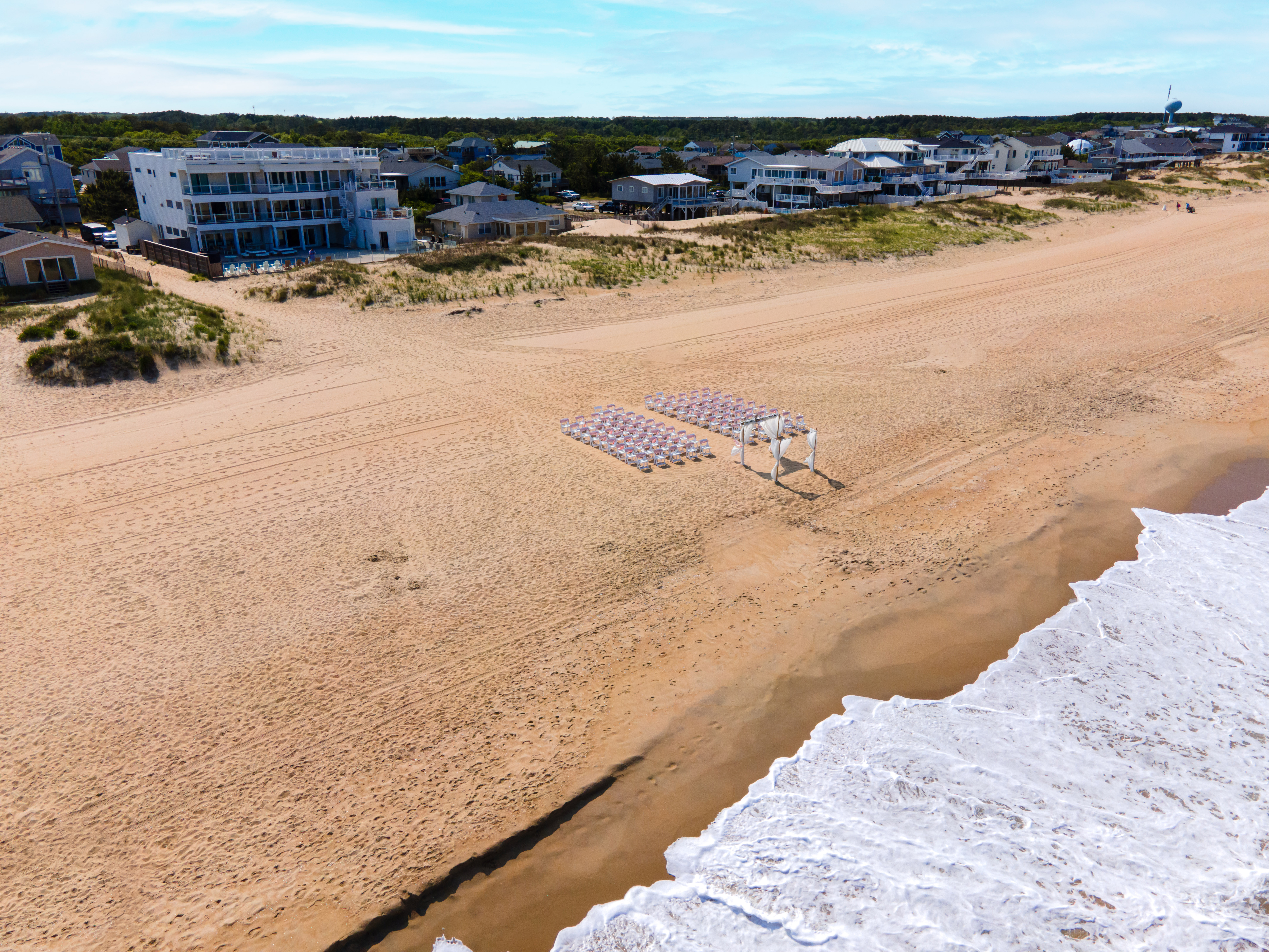 Aerial view of a beach with houses, chairs, and a canopy, showcasing the coastline and natural beauty.
